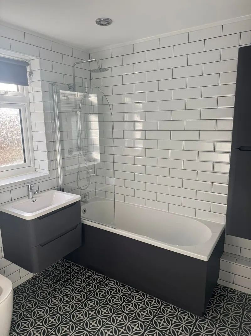 Bath with a bath screen and rainfall shower, surrounded by white metro tiles