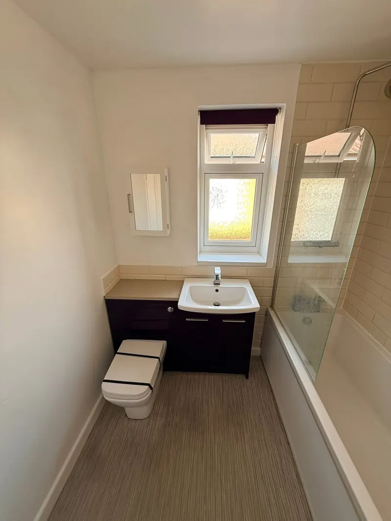 Bathroom before, with cream metro tiles, a purple vanity unit, and a bath with a bath screen