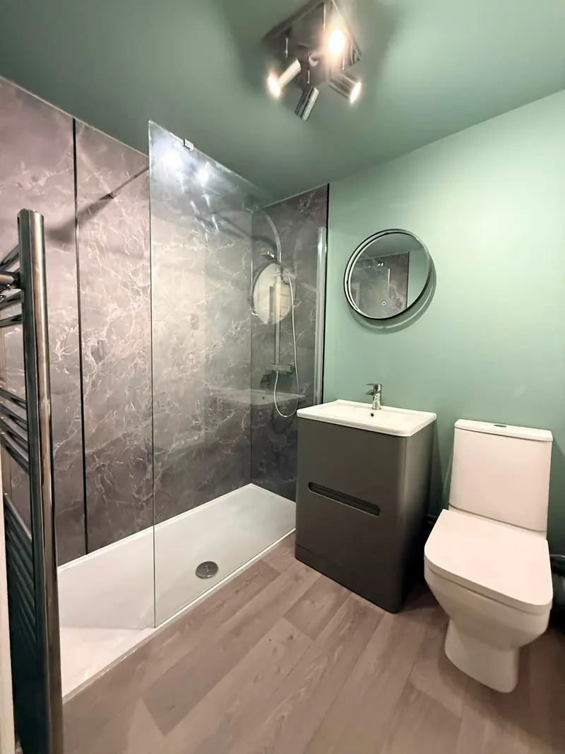 Walk-in shower with grey marble-effect wall panels, a grey vanity unit and a round mirror