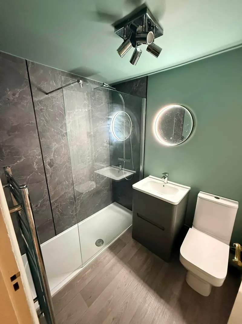 Shower room with a round LED mirror, a grey vanity unit and a chrome towel rail