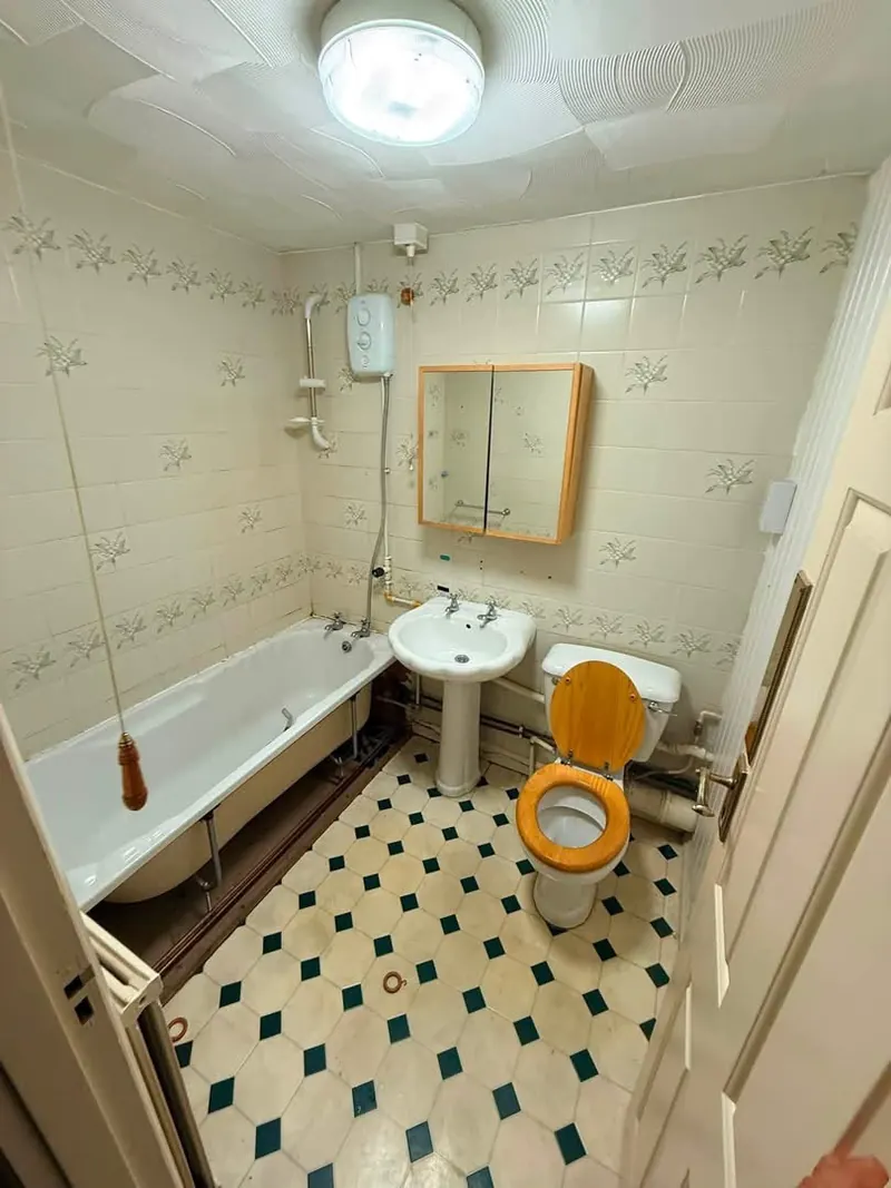 Bathroom before, with floral border tiles, a bath with an electric shower and a pedestal basin