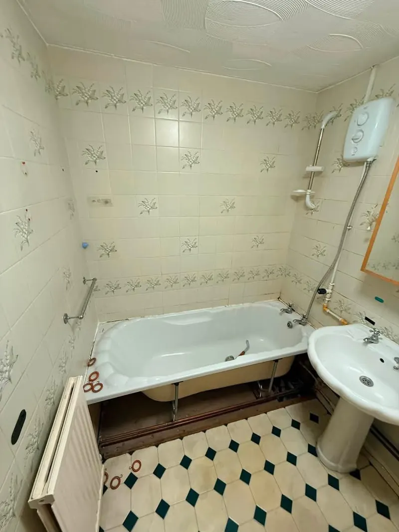 Bathroom before, with the bath panel off and exposed pipes under the bath