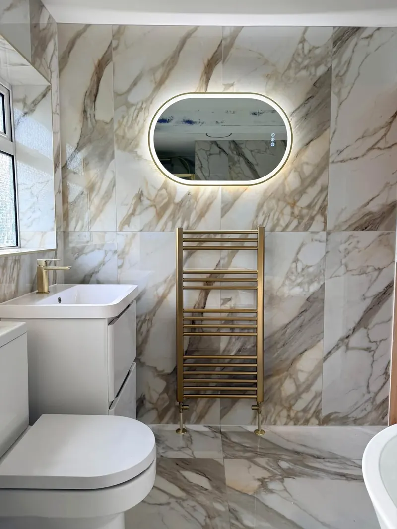 Oval LED mirror and brushed brass towel rail on marble-effect tiles