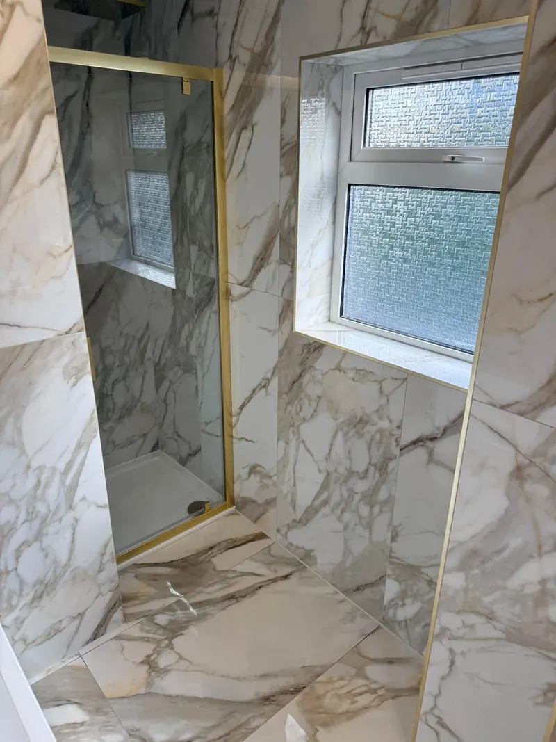 Brass-framed shower door and a tiled window reveal in marble-effect tiles