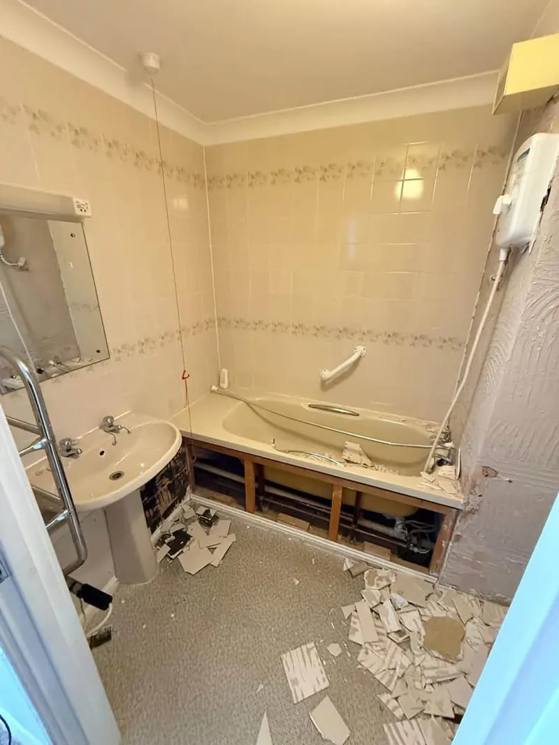 Old bathroom part stripped, with tiles on the floor and the bath panel off