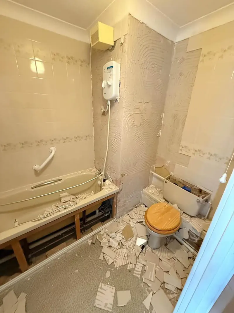 Old bathroom part stripped, with an electric shower over the bath