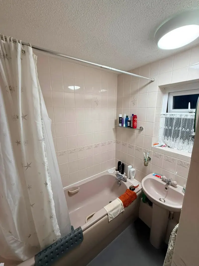 Bathroom before, with a pink bath and basin, pink tiles and a shower curtain