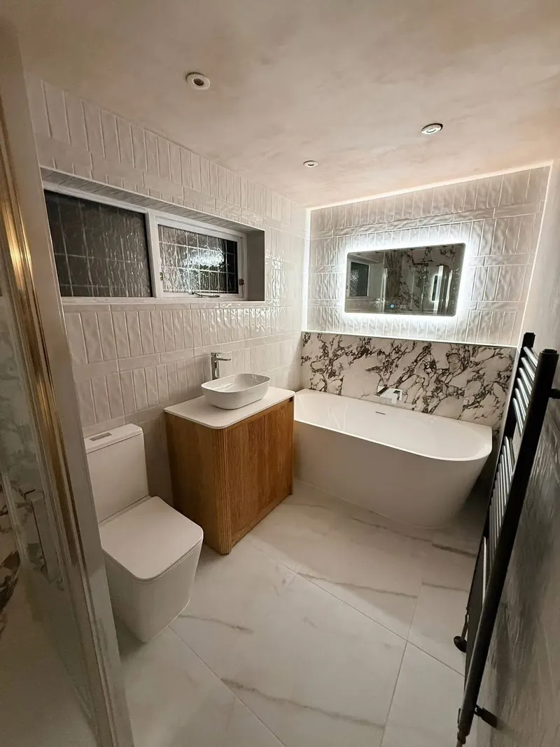 Finished bathroom with a back-to-wall bath, an LED mirror, a marble-effect splashback and a fluted wood vanity unit