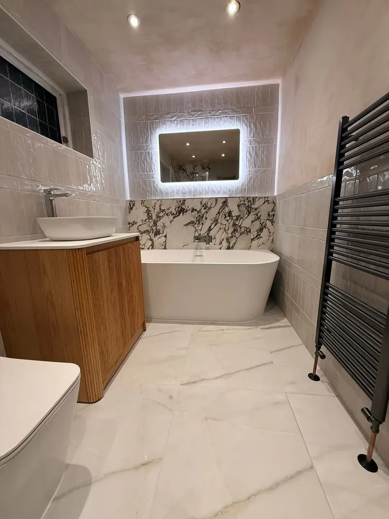 Fluted wood vanity with a countertop basin next to a back-to-wall bath and a dark grey towel rail