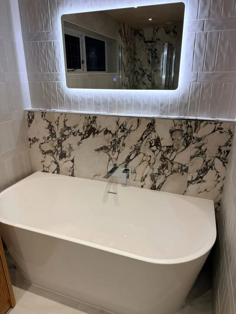 Back-to-wall bath with a wall-mounted tap, a marble-effect splashback and an LED mirror