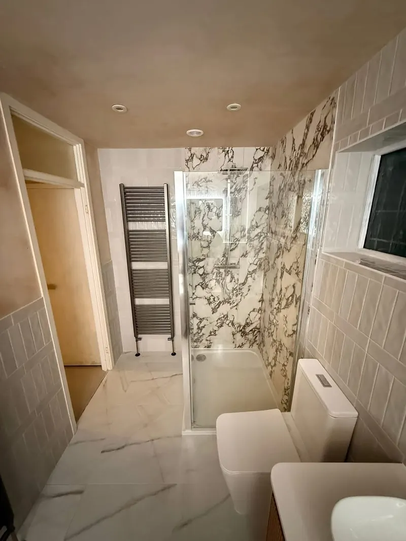 Shower enclosure with marble-effect walls and a tall dark grey towel rail by the door