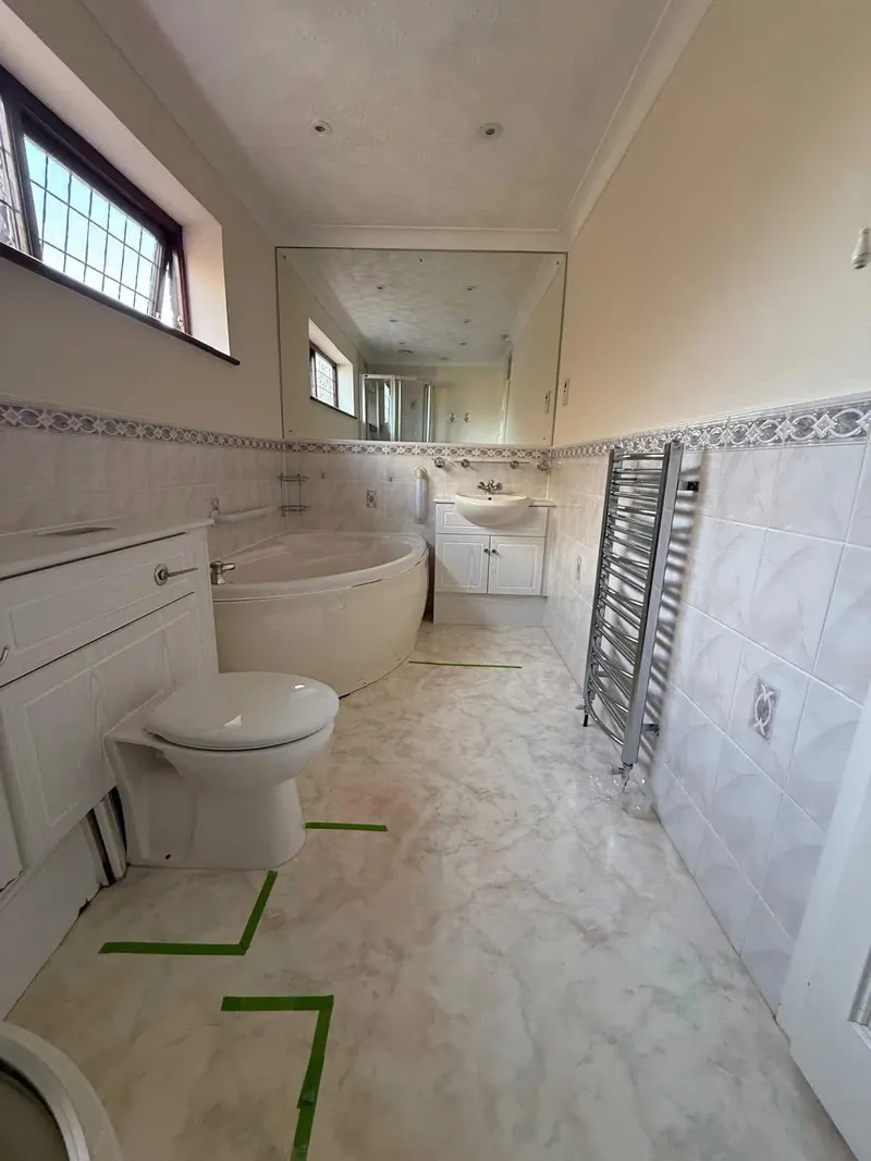 Long bathroom before, with a corner bath, a vanity unit, a large wall mirror and a chrome towel rail
