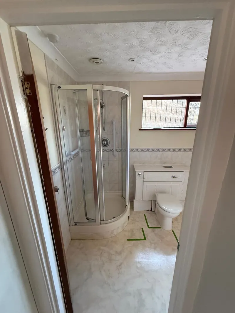 The same bathroom before, with a curved corner shower cubicle and a toilet unit, seen from the door