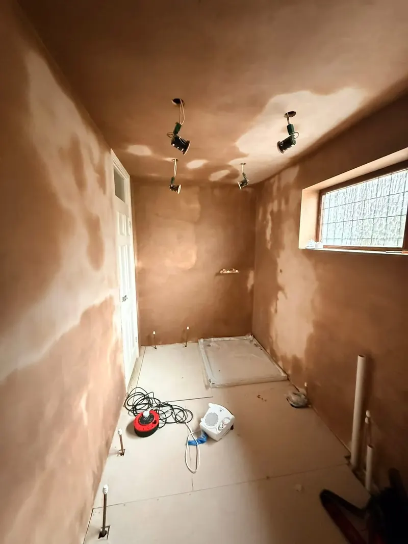 The same room stripped back to fresh plaster, with the new shower tray in place and pipes ready for the new bathroom