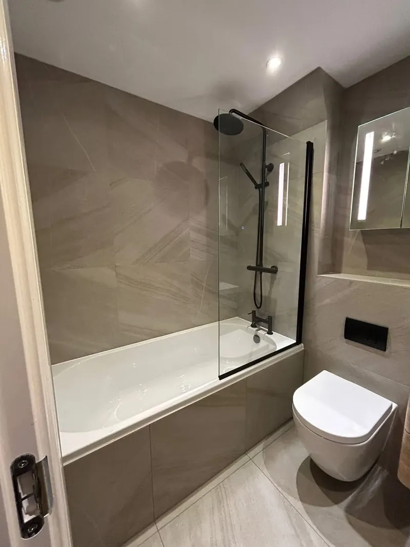 Renovated bathroom with large stone-effect tiles, a tiled bath panel, a black shower and a wall-hung toilet