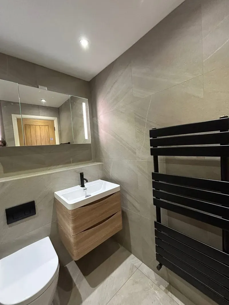 Wood-effect wall-hung vanity, black tap and a black towel rail on stone-effect tiles