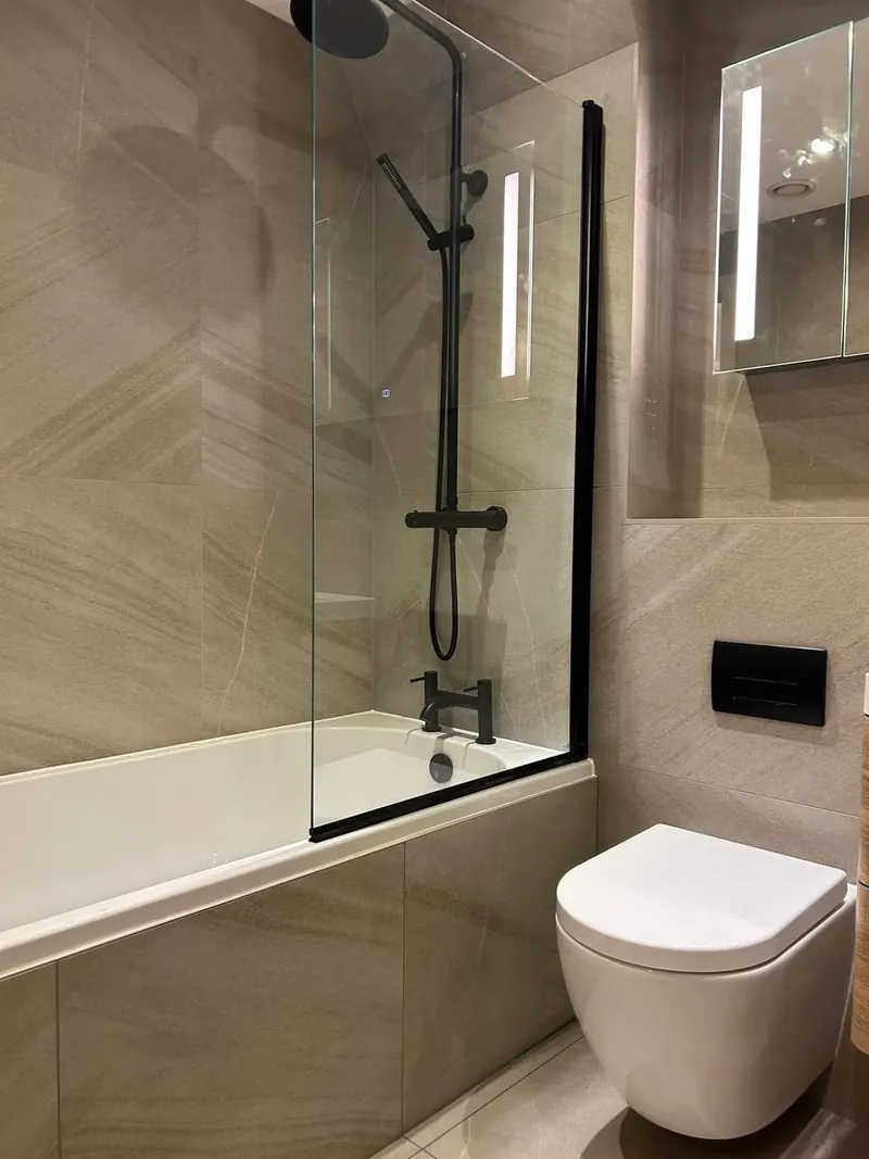 Bath with a bath screen and a black shower, in large stone-effect tiles