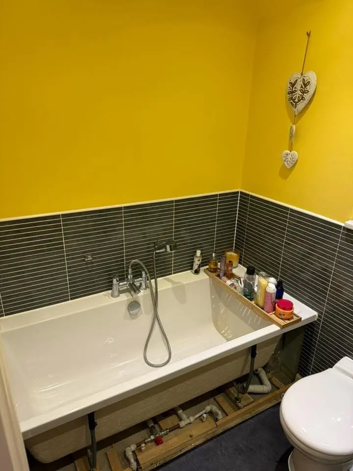Bathroom before, with yellow walls, dark grey strip tiles and the bath panel off
