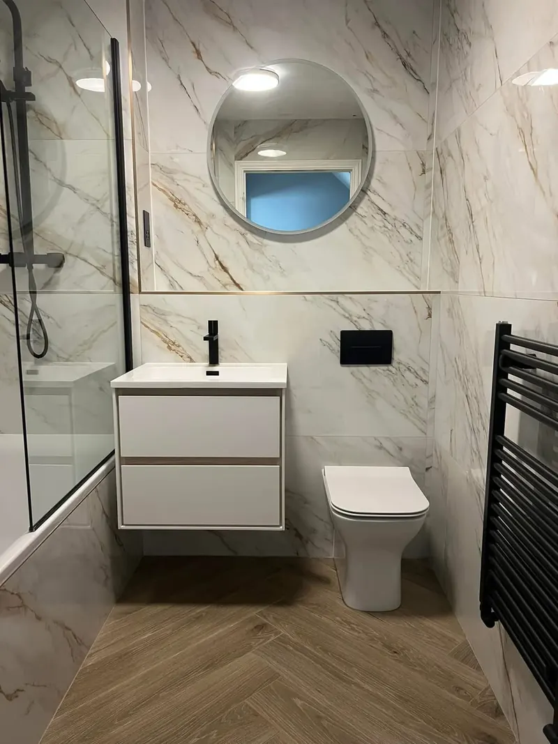 Renovated bathroom with gold-veined marble-effect tiles, a white wall-hung vanity, a round mirror and a herringbone floor
