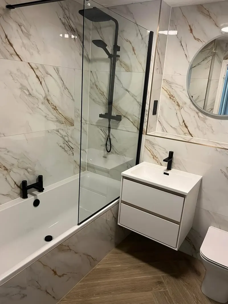 Bath with a black shower and a bath screen, in gold-veined marble-effect tiles