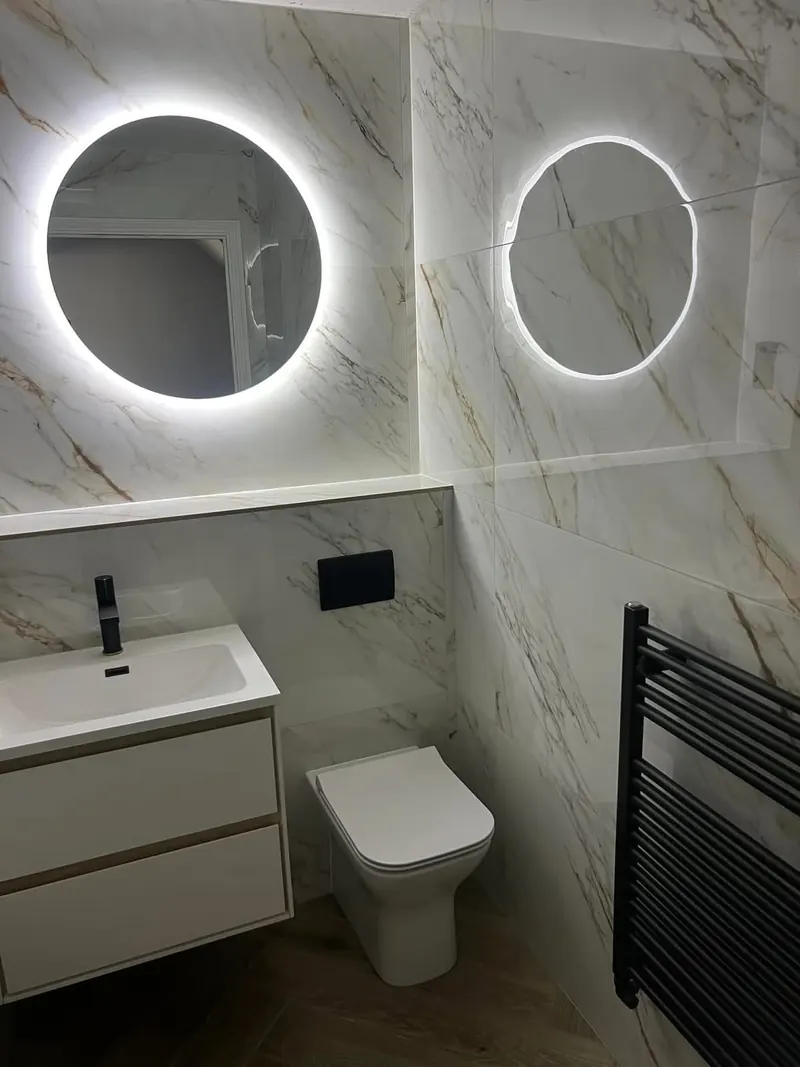 Round LED mirror, vanity unit and toilet in a marble-effect bathroom