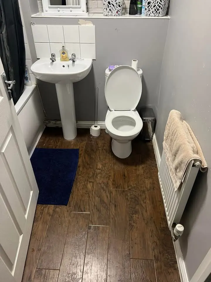 Bathroom before, with a dark wood-effect floor and a radiator