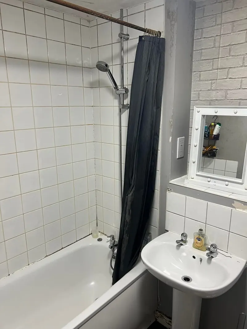 Bath before, with a shower curtain, white tiles and dark grout